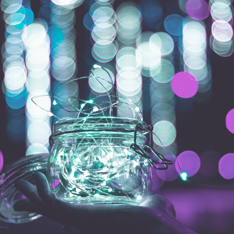 Hand holding a jar of white fairy lights against a background of blurred white, blue, and purple lights