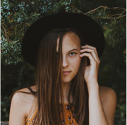 person with long brown hair wearing black hat tucking hair behind their ear