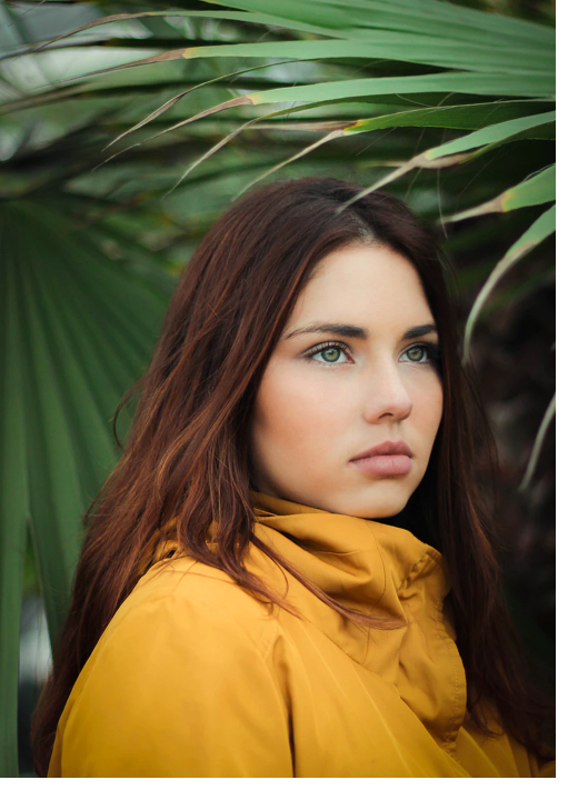 photo of Willow in a mustard yellow jacket with palm leaves in the background
